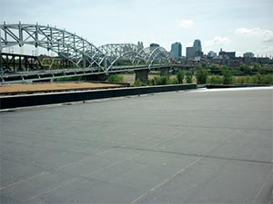 EPDM-Roofing-Kettering-OH-Ohio-2 | A.H. Sturgill Roofing Paved waterfront area with a large steel truss bridge over a river and a distant city skyline in the background.