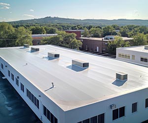 TPO-Roofing-Kettering-OH-Ohio-2 | A.H. Sturgill Roofing Aerial view of a large white flat-roofed commercial building with several rooftop HVAC units, surrounded by trees and other low buildings.