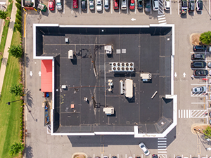 EPDM-Roofing-Beavercreek-OH-Ohio-2 | A.H. Sturgill Roofing Aerial view of a U-shaped commercial building with a black roof, white exterior, and surrounding parking lots full of cars while a few trees line the street edges.